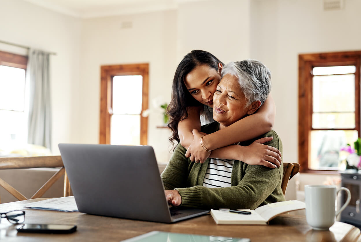 Young woman hugging her elderly mother while looking at a laptop, representing life insurance services - Cardinal Life.